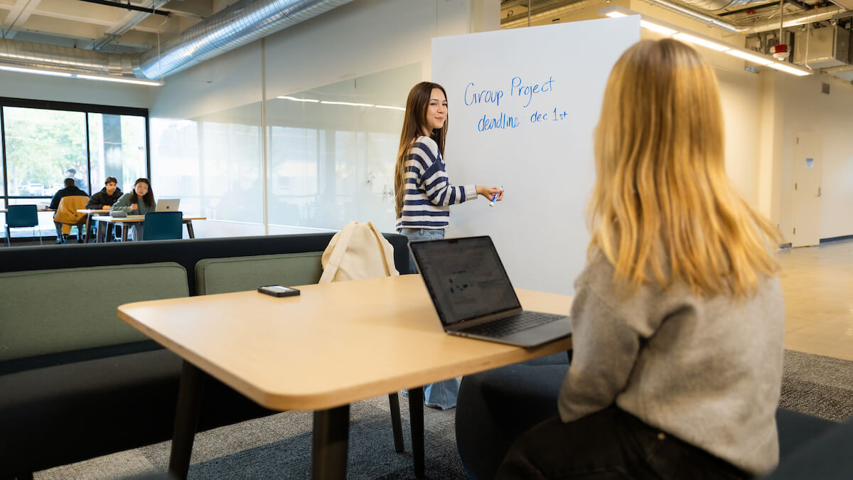 Students at the library in a room with a whiteboard and a laptop