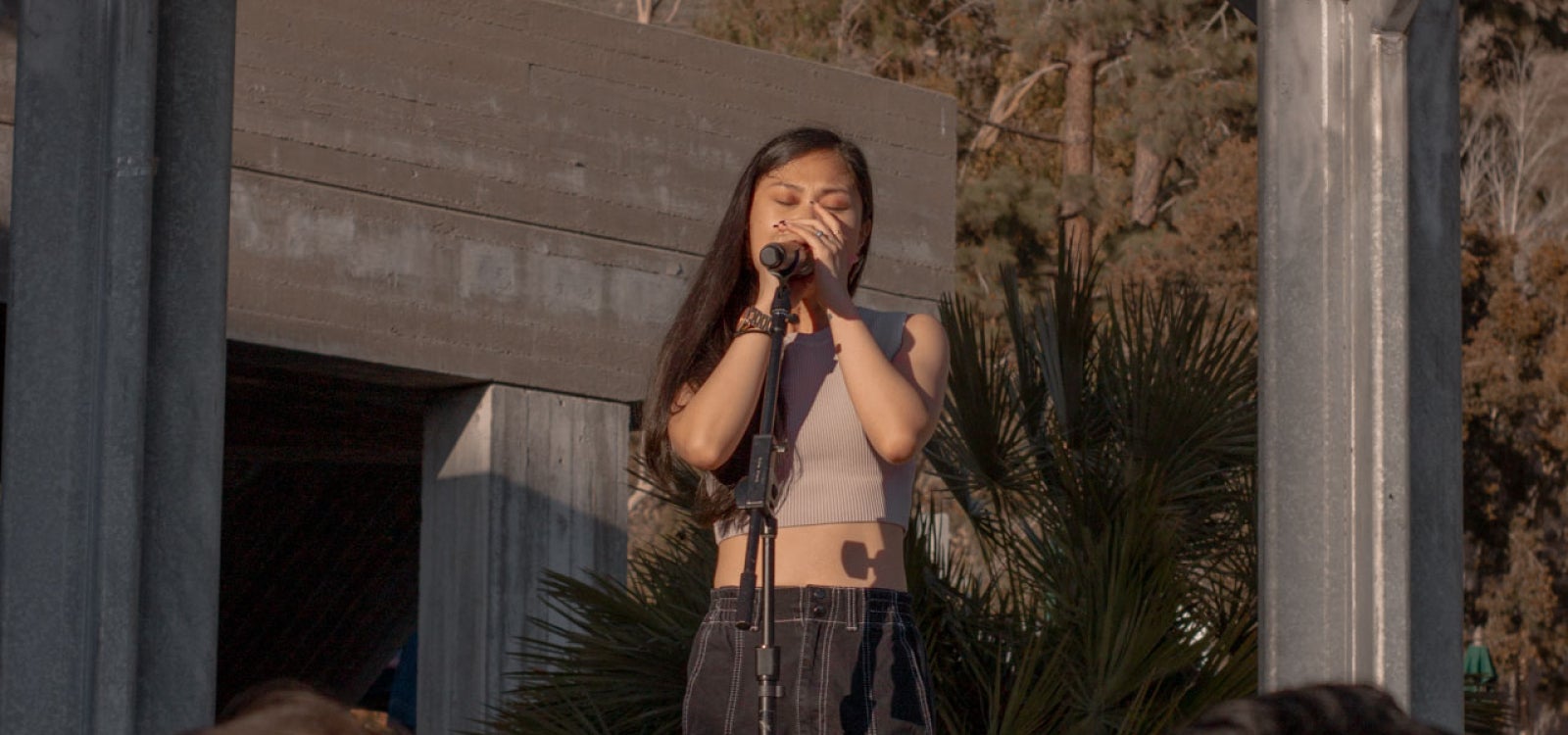 Ruby Ibarra, wearing a tan crop top and dark baggy pants, holding the microphone and singing on the University Union Stage