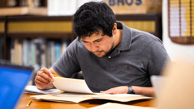 Student reading a book at the Santa Barbara Mission for a History Class