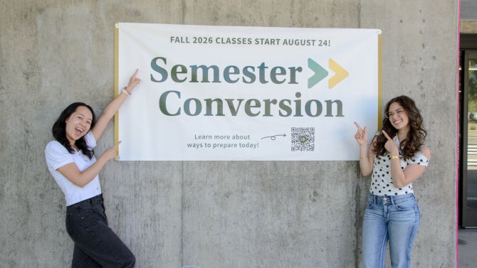 Two students stand next to a Semester Conversion sign